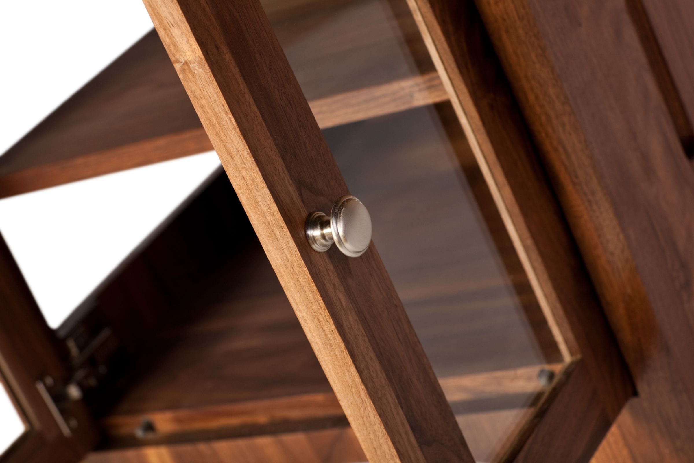 Close-up of a brushed-steel knob on a glazed walnut cabinet door