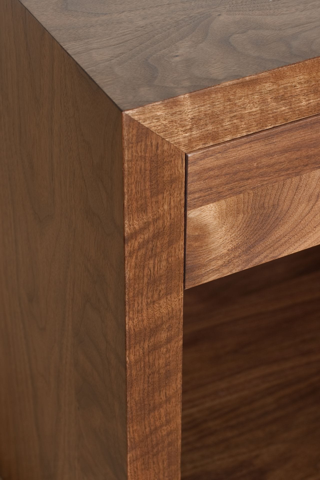 Corner detail of a walnut cabinet showing figured grain and crisp mitred edges