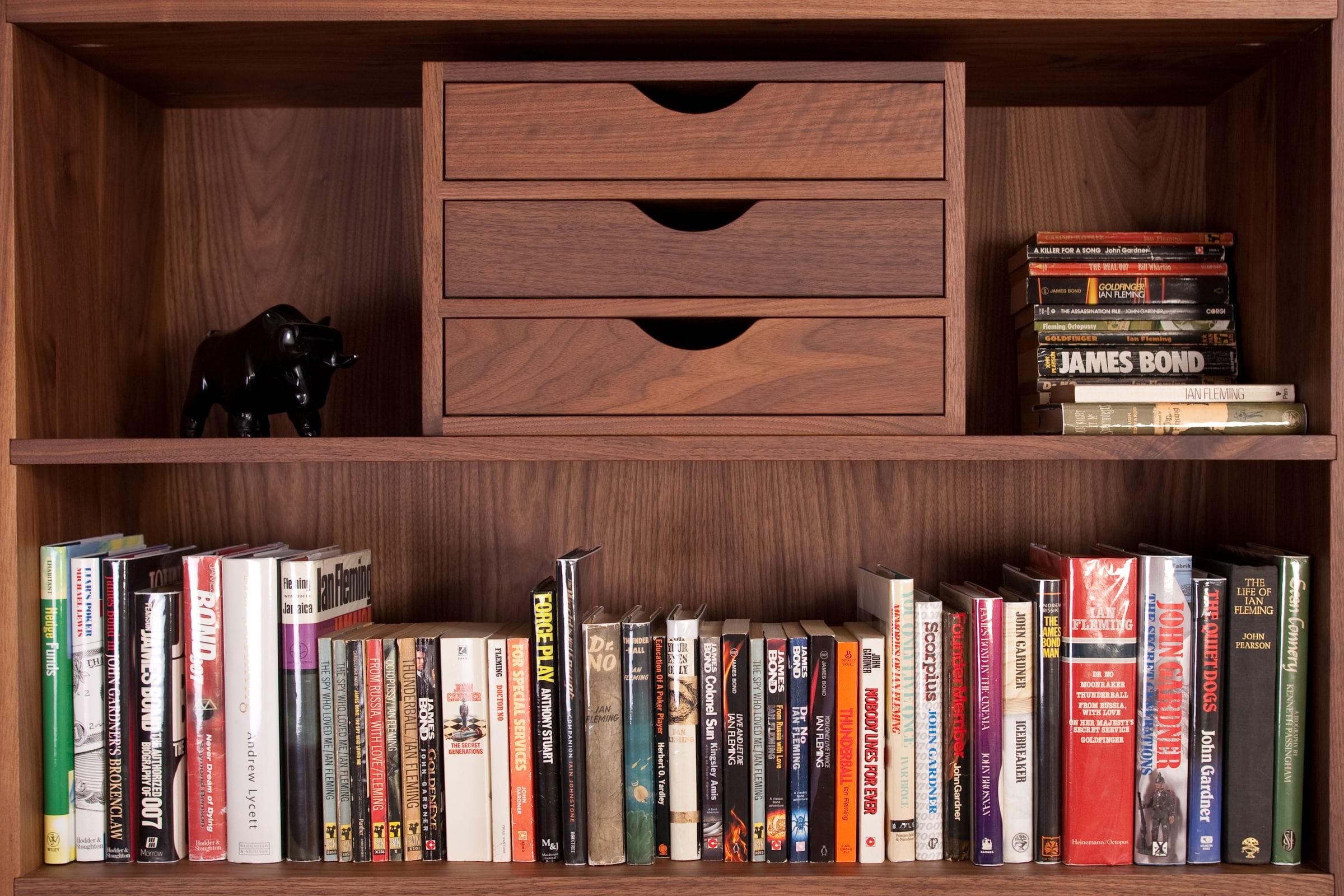 Walnut shelves holding a three-drawer desk tidy, paperback novels and a bull ornament