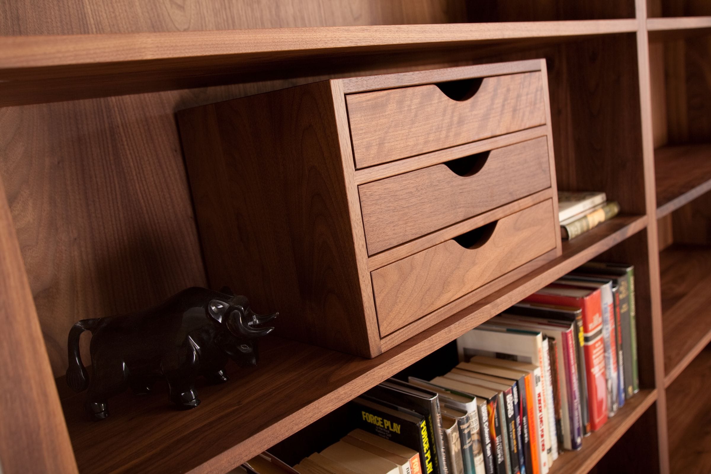 Three-drawer walnut desk tidy on a bookshelf beside a black elephant ornament