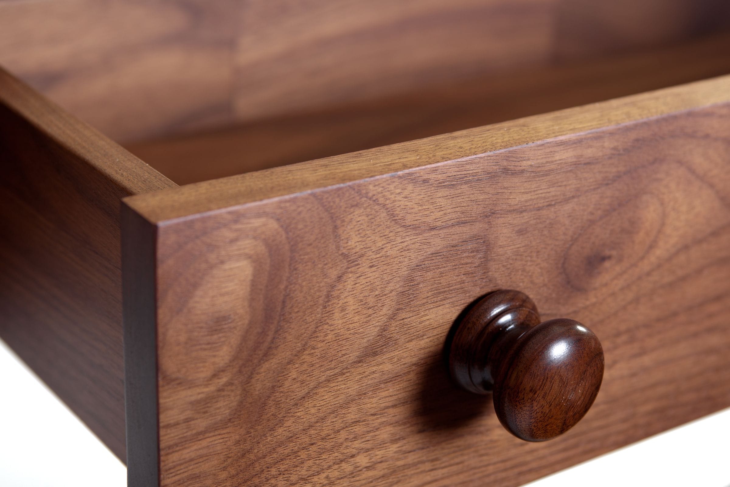 Close-up of a turned walnut knob on an open drawer with figured grain
