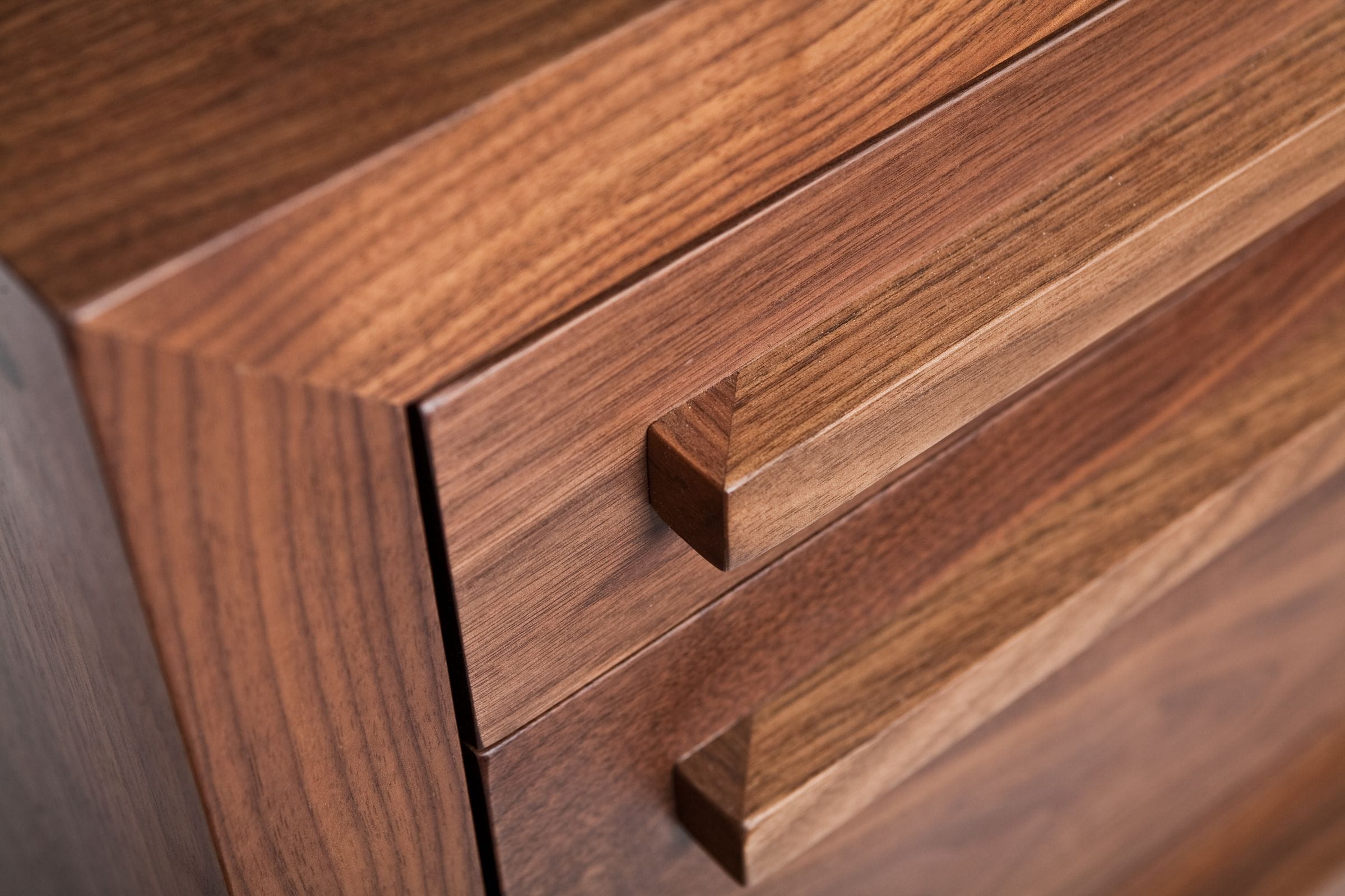 Close-up of slim walnut drawer handles and rich grain on a chest of drawers