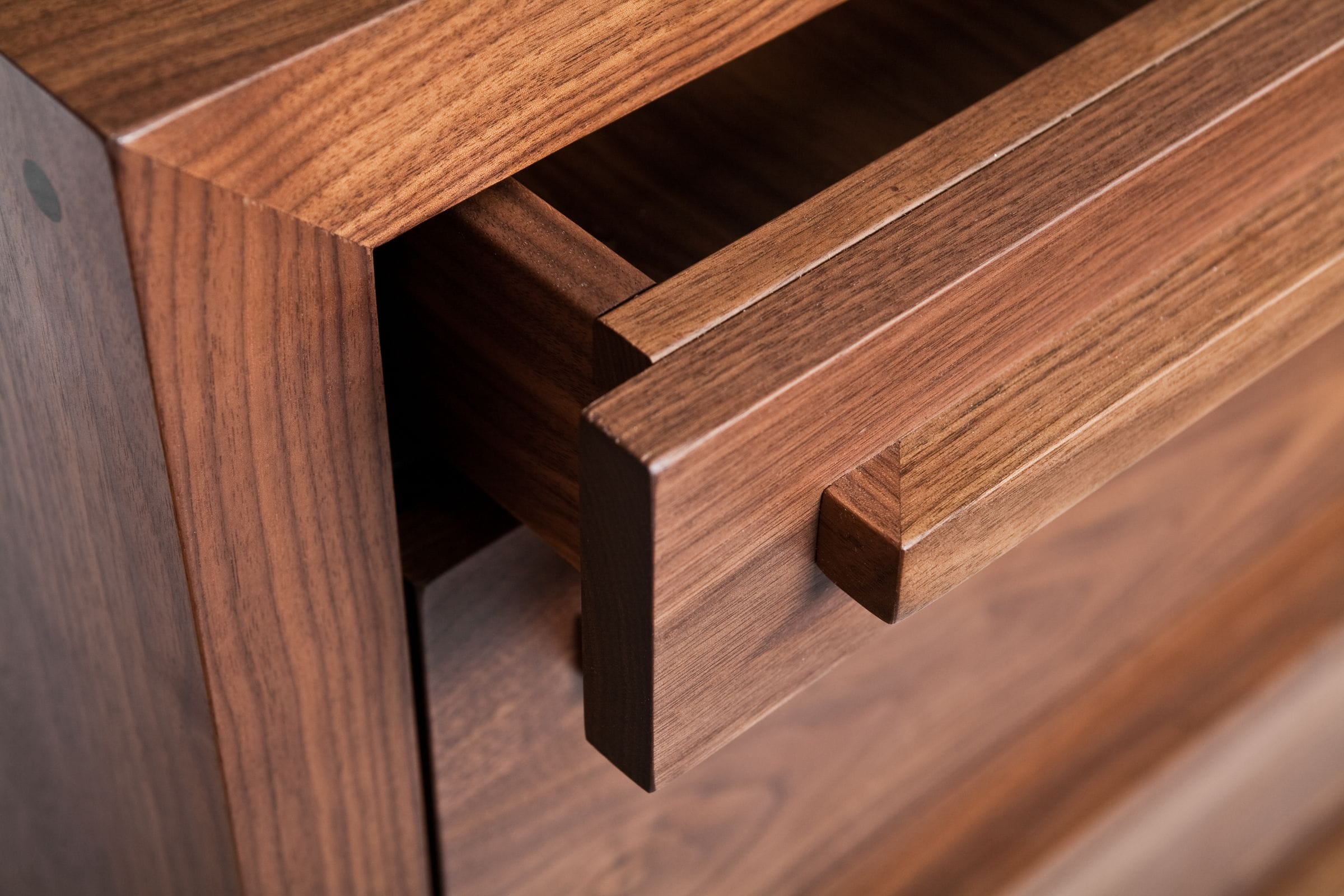 Detail of an open walnut drawer front with integrated wooden handle