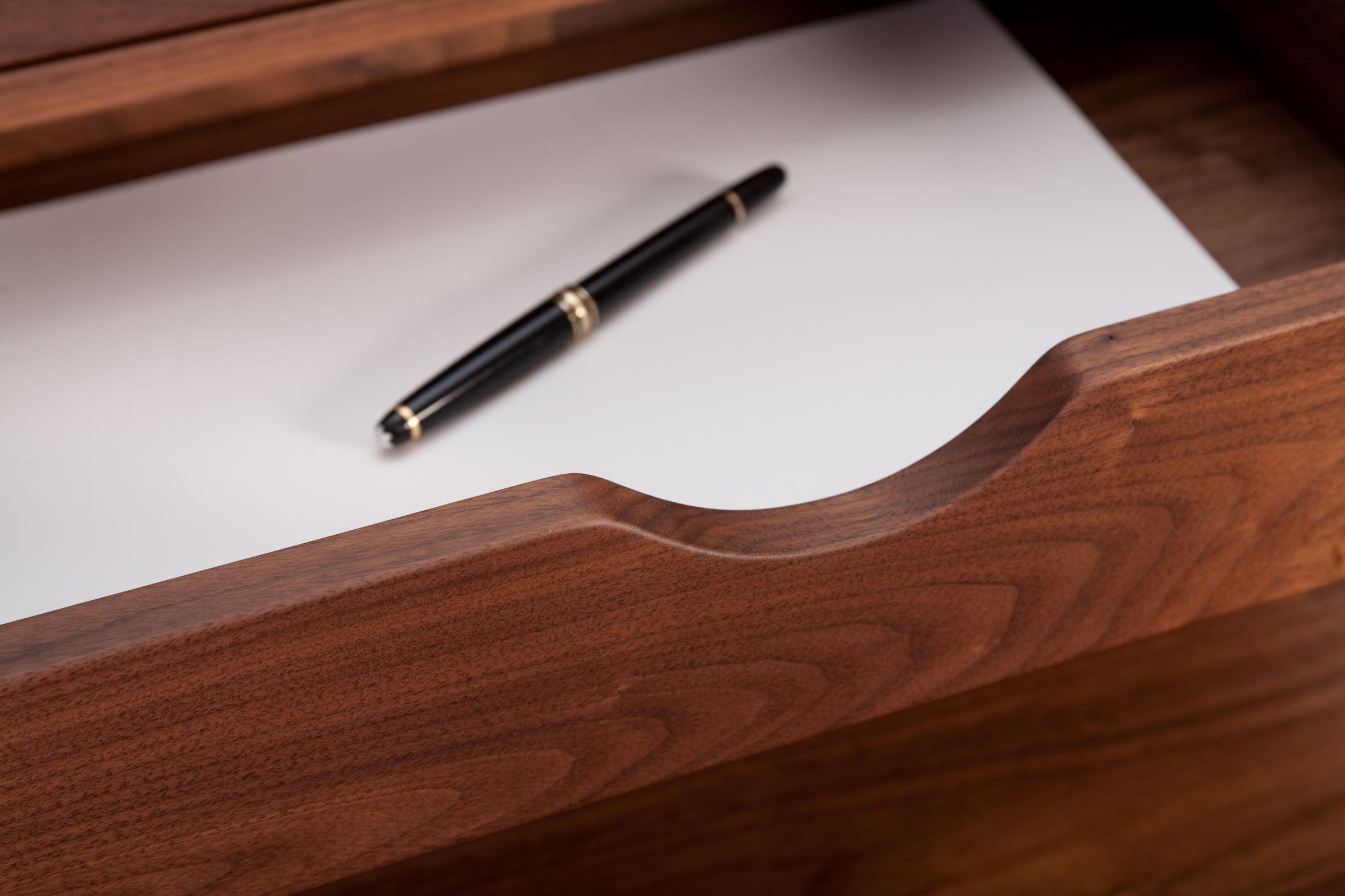 Close-up of a walnut drawer's curved cut-out with paper and a fountain pen inside