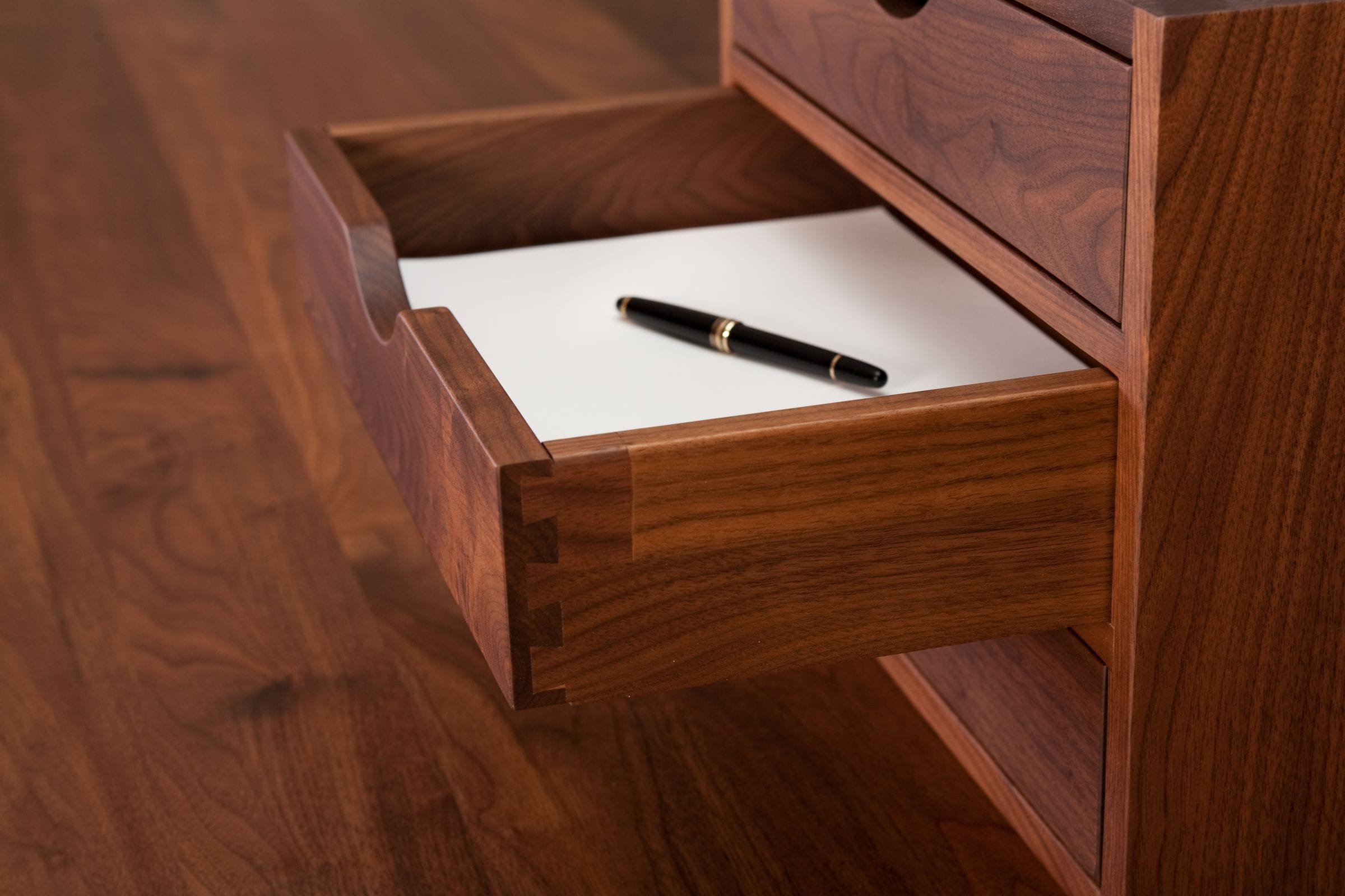 Open walnut drawer with dovetail joints holding paper and a fountain pen
