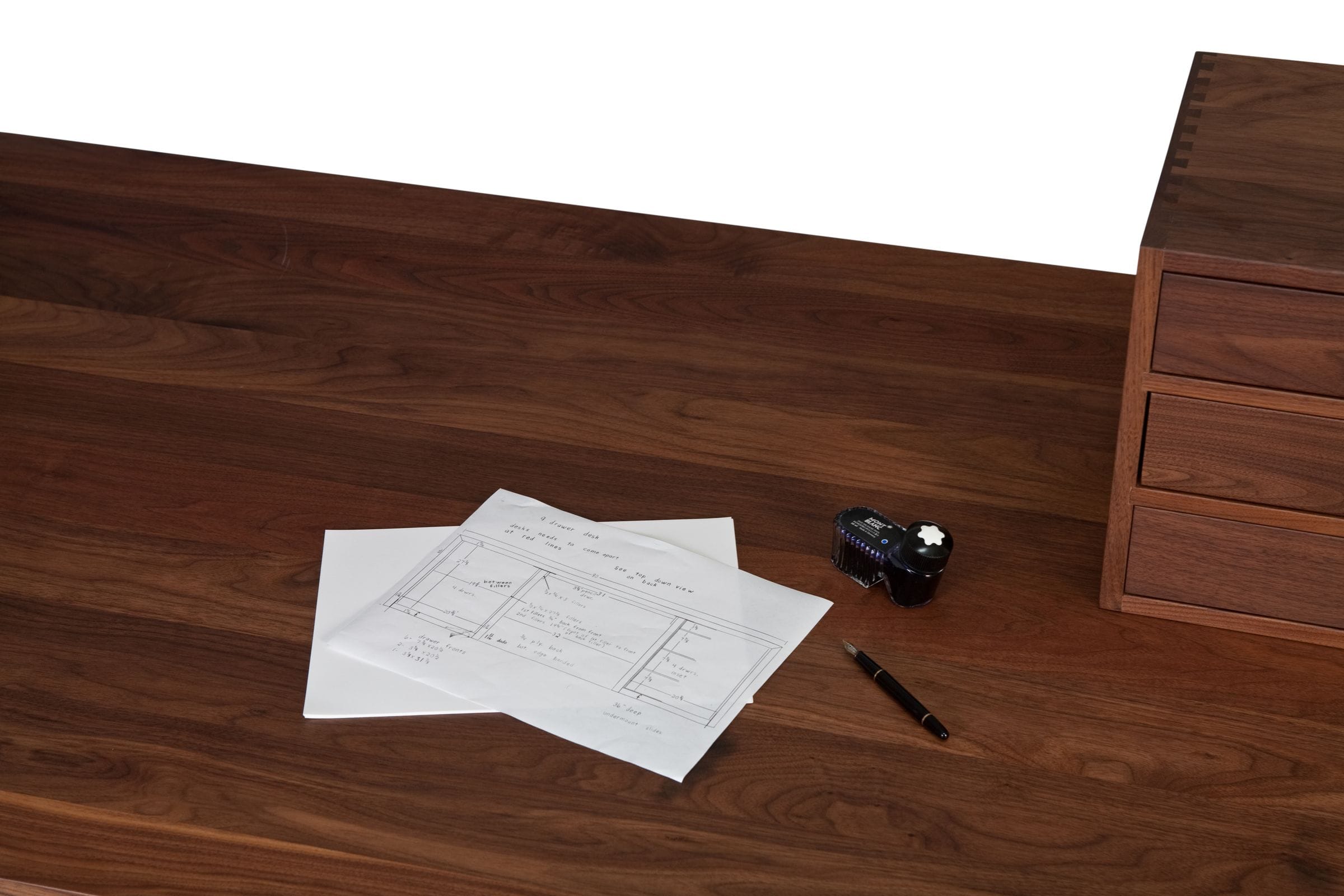 Walnut desk top with handwritten plans, fountain pen, ink bottle and small drawer unit