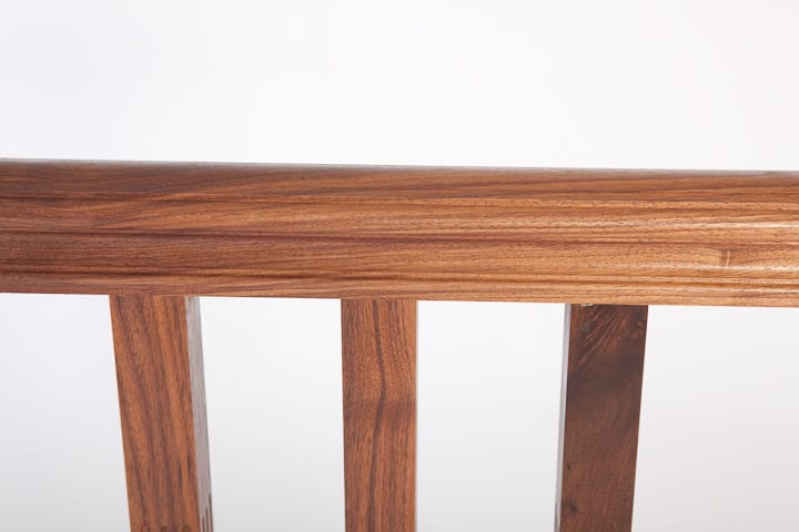 Close-up of a walnut bench backrest rail and square spindles