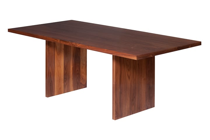 Angled view of a solid walnut dining table with wide panel legs