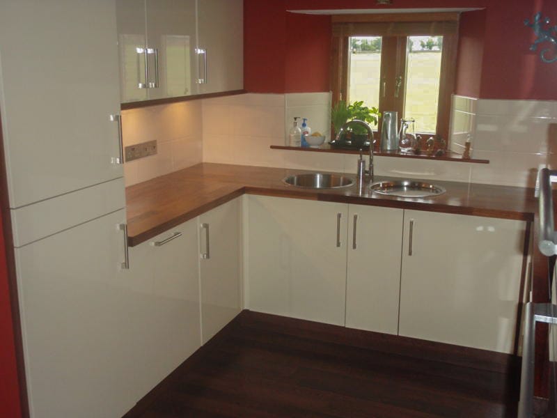 Walnut worktops with inset stainless sinks in a cream gloss kitchen with red walls