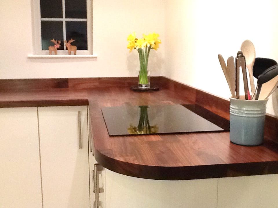 Curved walnut worktop with inset black hob, daffodils and utensil pot in a cream kitchen