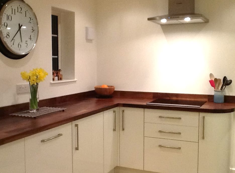 L-shaped walnut worktops in a cream kitchen with wall clock and daffodils