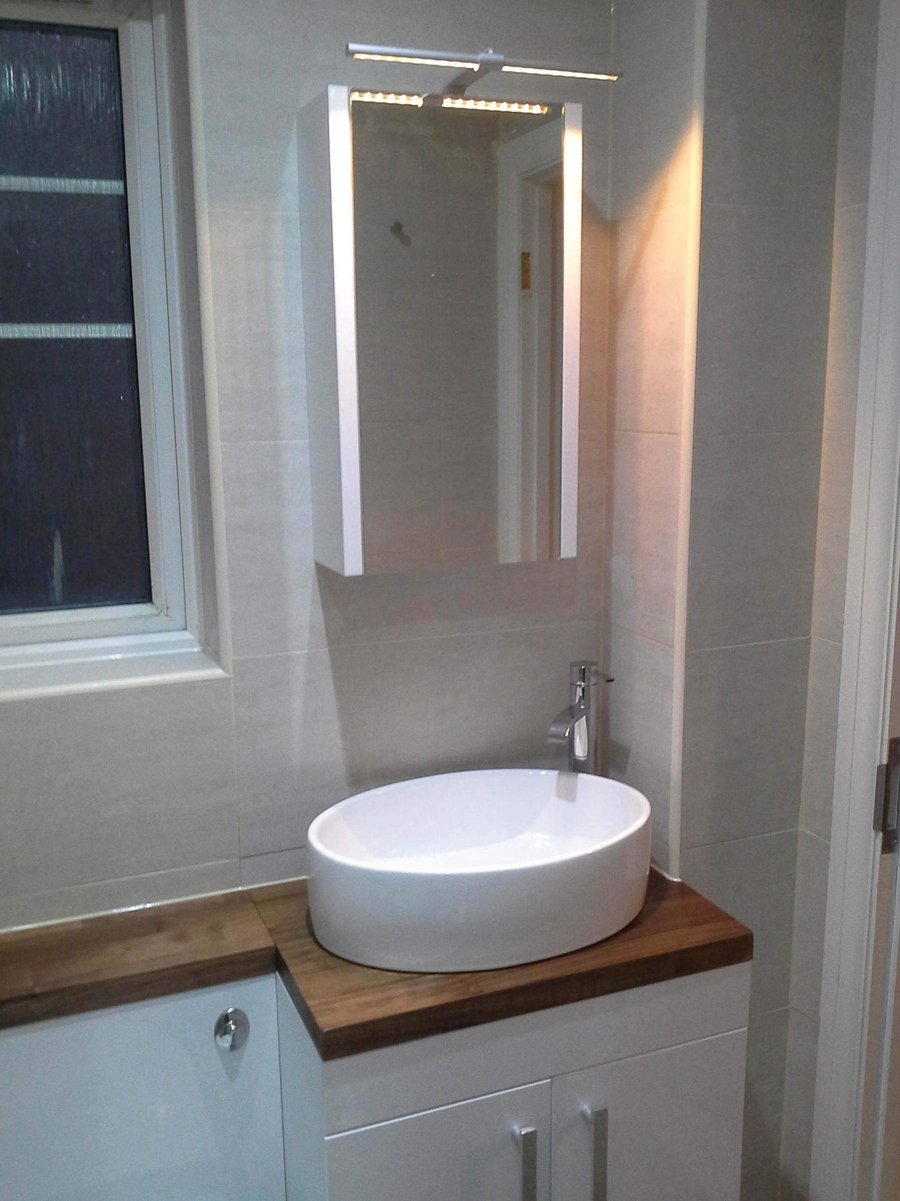 Walnut vanity top with oval countertop basin in a tiled bathroom