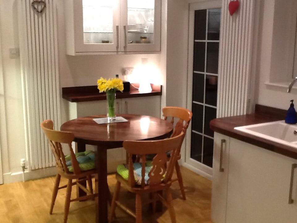 Round walnut dining table with pine chairs and daffodils beside a walnut worktop