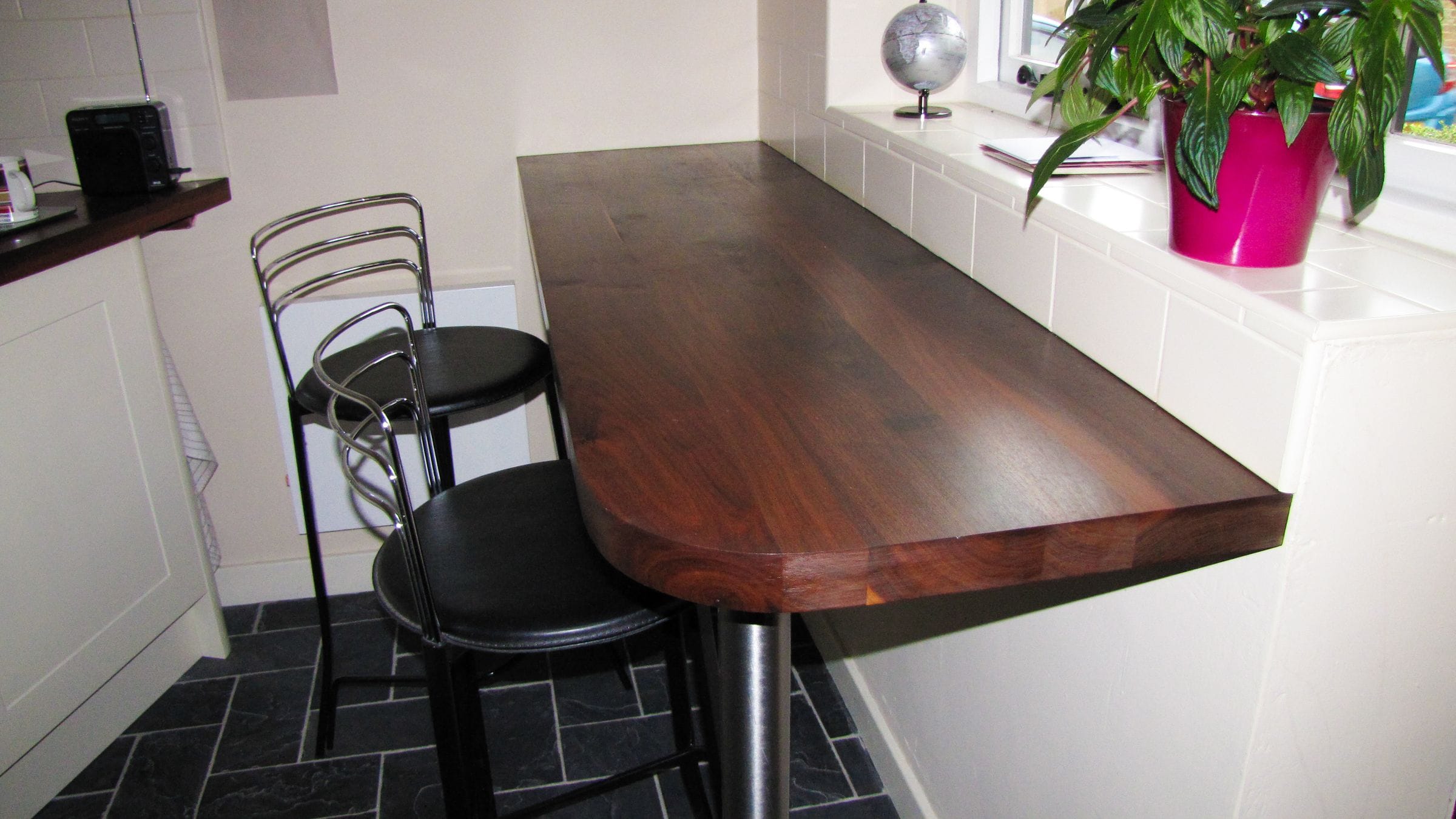 Walnut breakfast bar with rounded corner and black bar stools on slate tiles