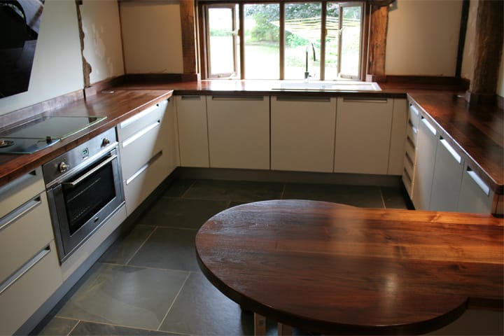 Oval walnut breakfast bar in a U-shaped cream kitchen with exposed beams