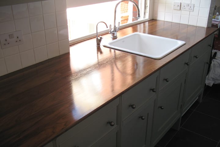 Polished walnut worktop with white inset sink on sage green cabinets
