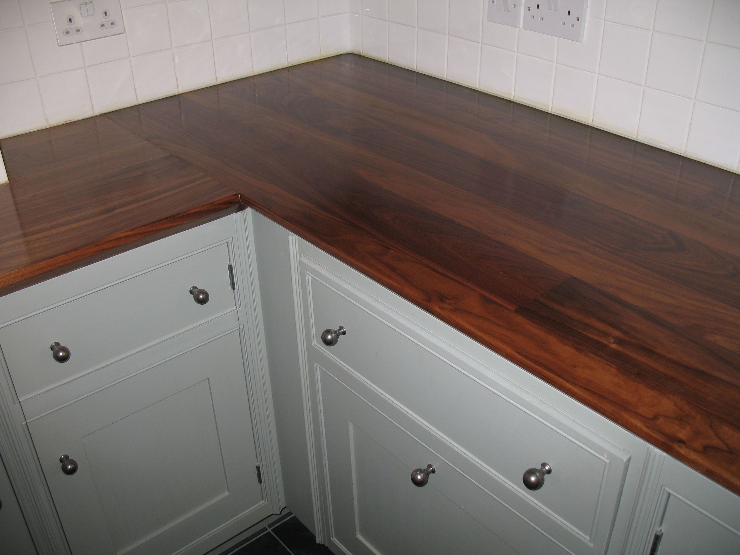 Corner detail of a rich walnut worktop over pale blue painted cabinets