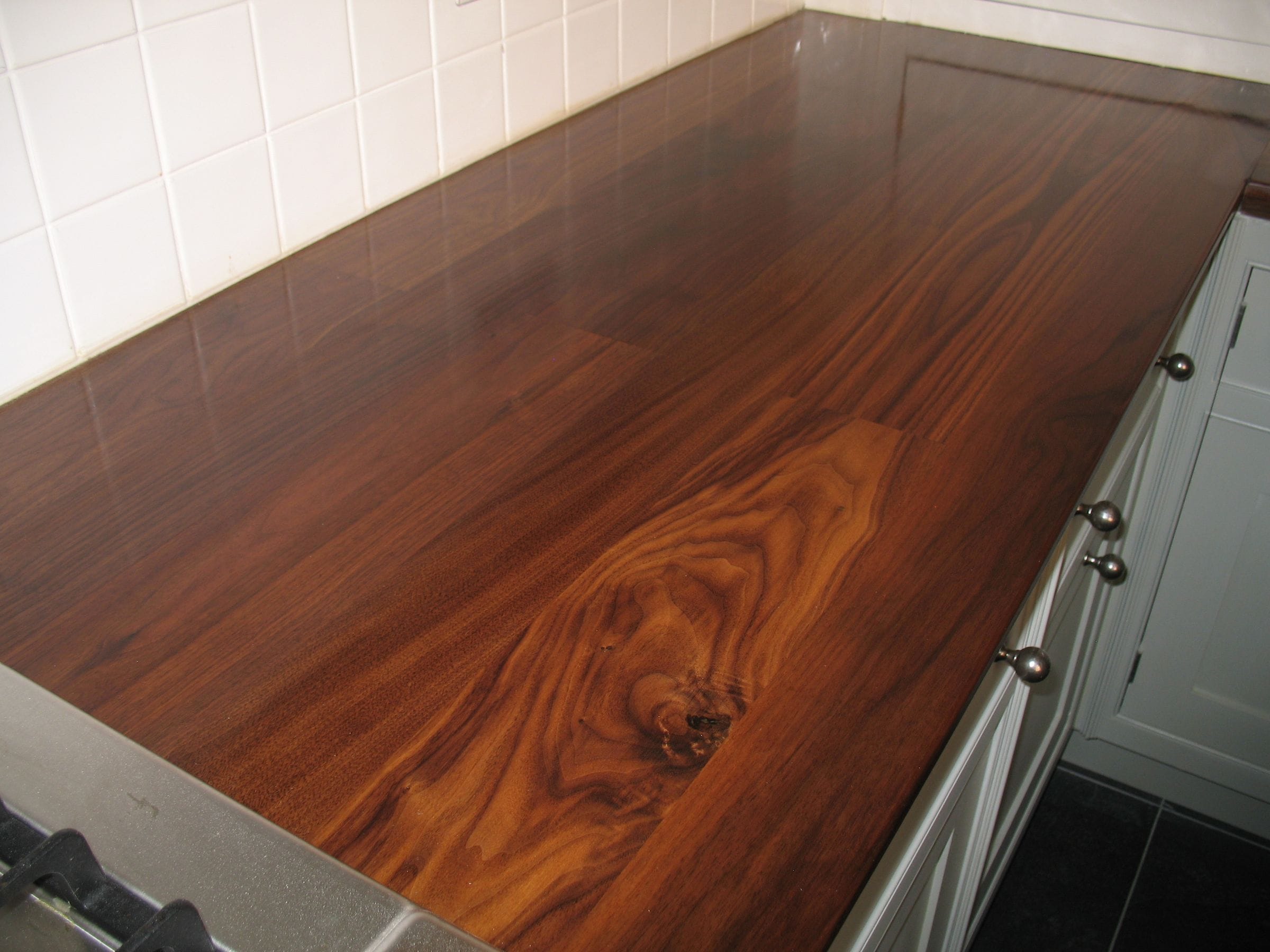 Figured walnut worktop with distinctive knot against white wall tiles