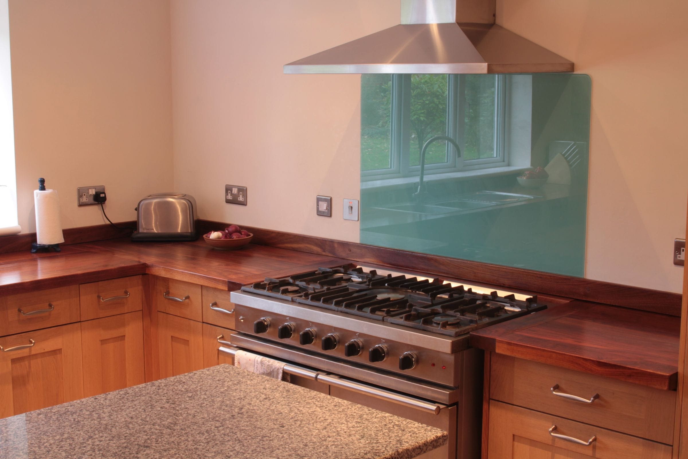 Walnut worktops flanking a range cooker with green glass splashback and chimney hood