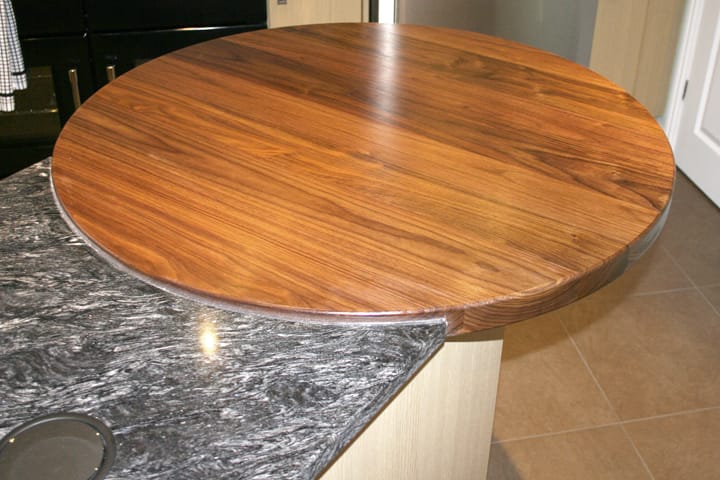 Circular walnut breakfast bar overhanging a grey granite kitchen island