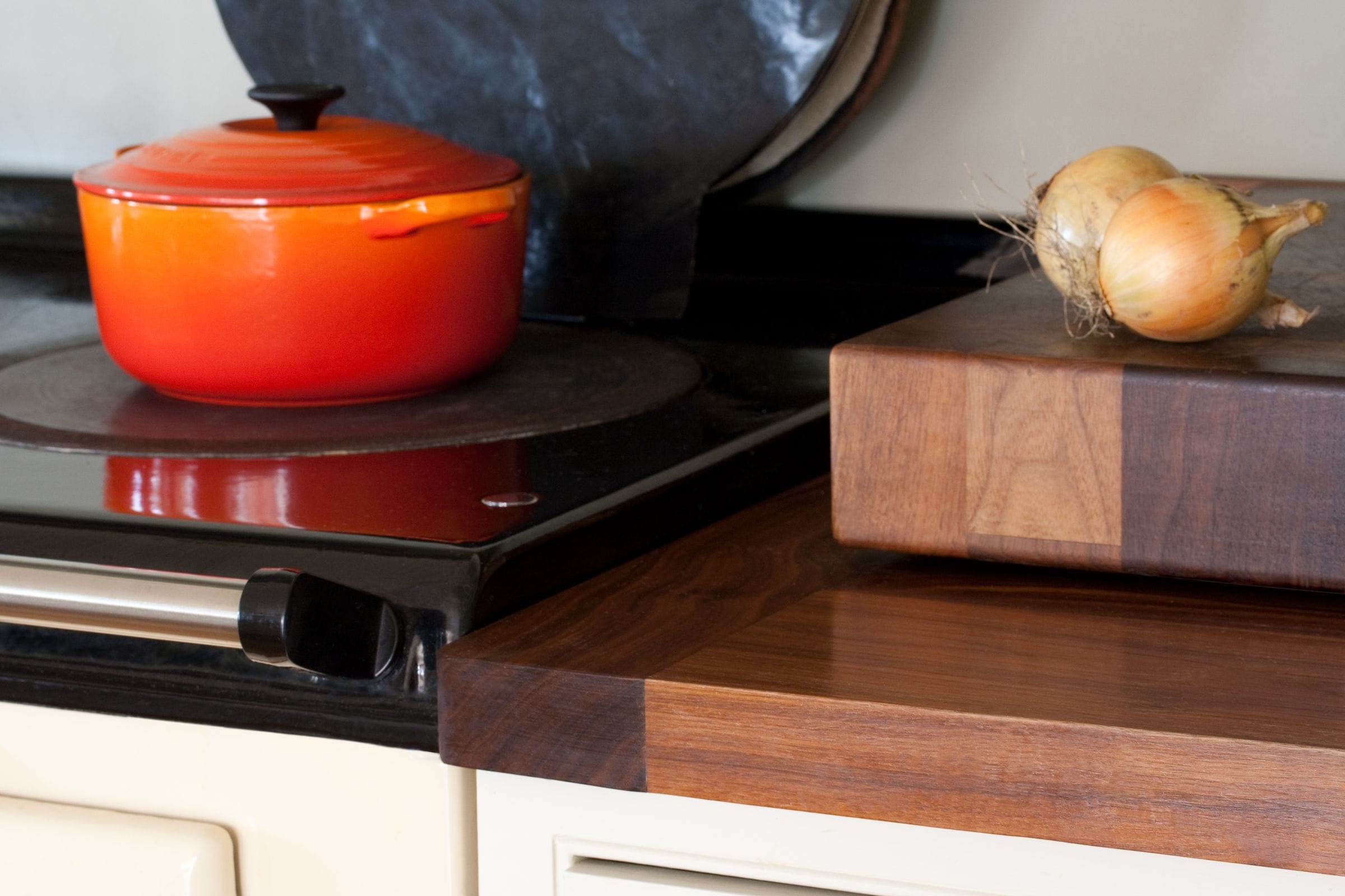End-grain walnut butcher block on a worktop beside a range cooker with orange casserole