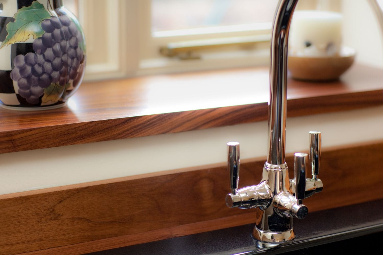 Chrome three-lever tap against a walnut window sill and upstand