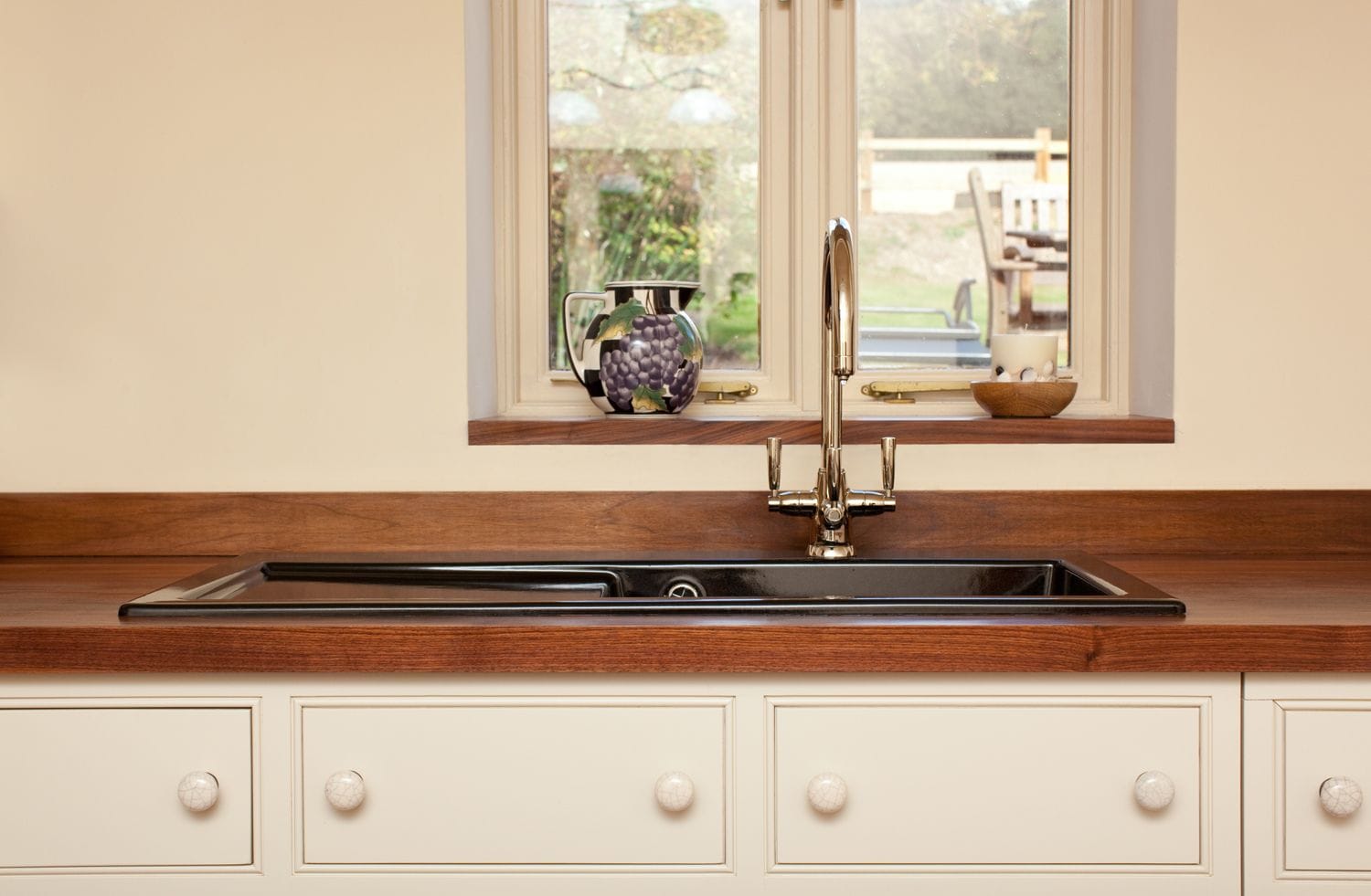 Black inset sink with drainer grooves in a walnut worktop below a cottage window