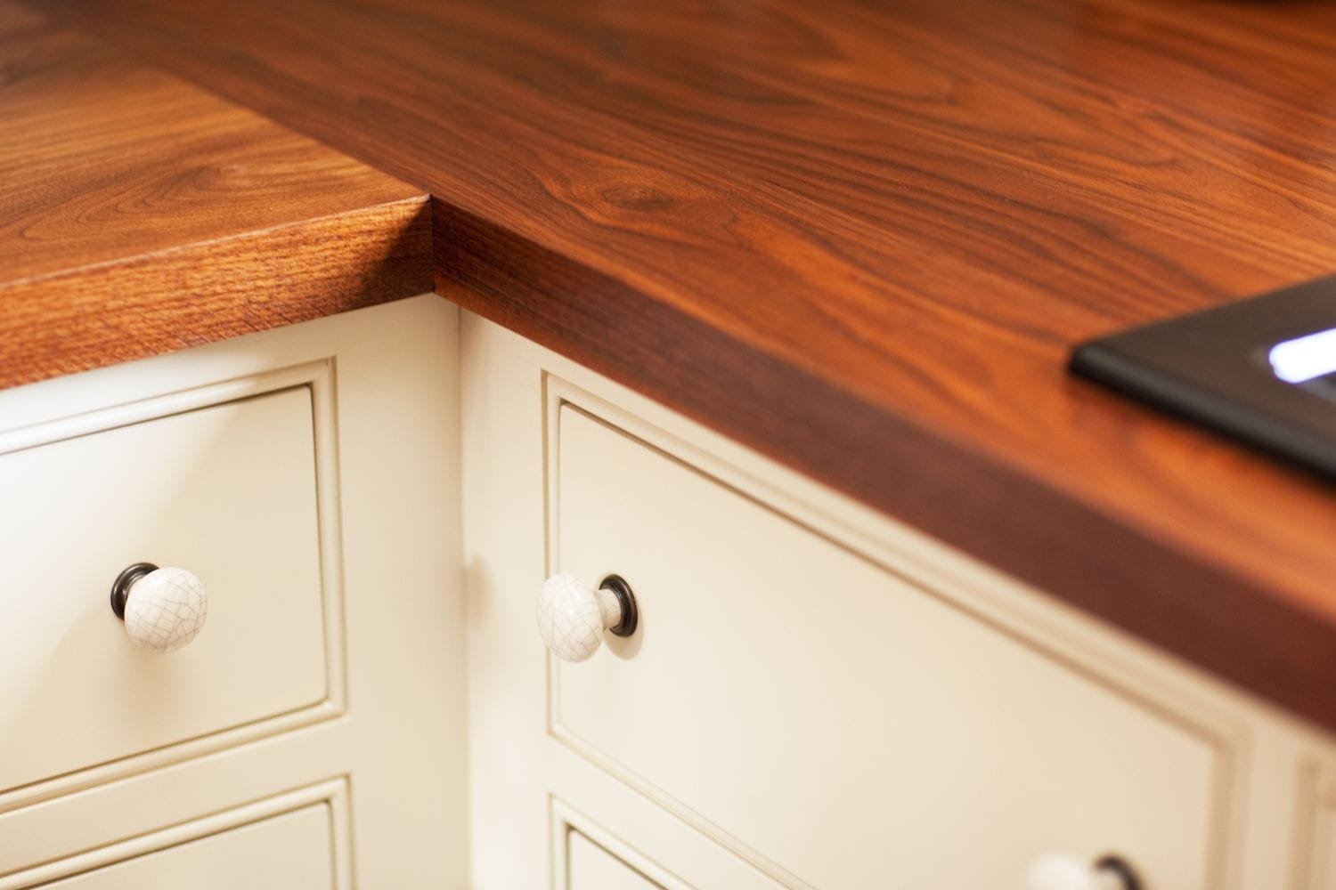 Corner of a walnut worktop over cream drawers with ceramic knobs