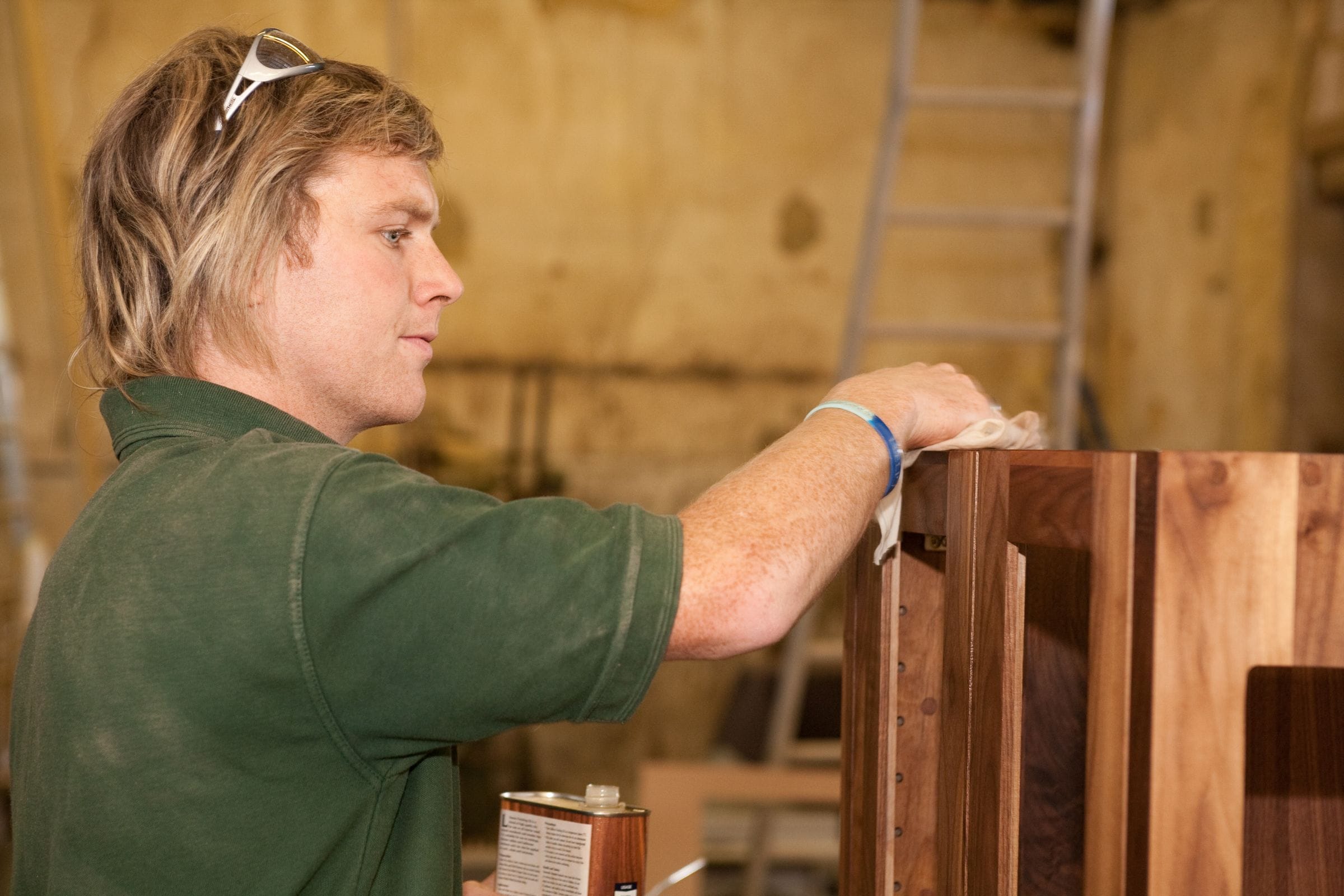 Craftsman hand-finishing a walnut cabinet with oil in the workshop