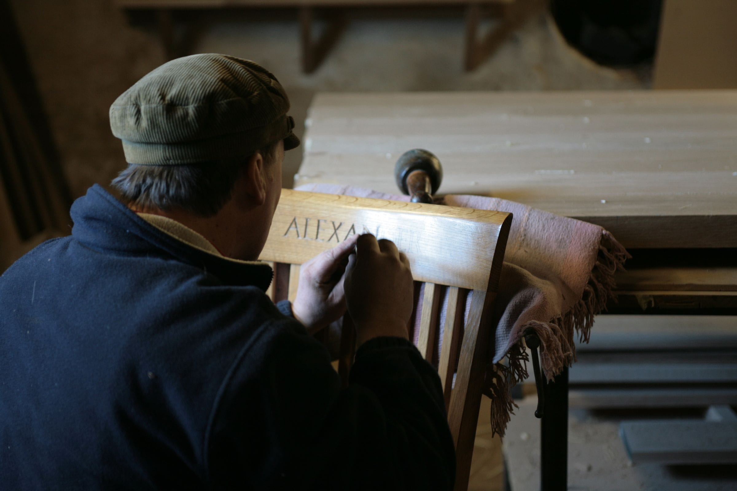 Craftsman hand-carving lettering into an oak chair back in the workshop