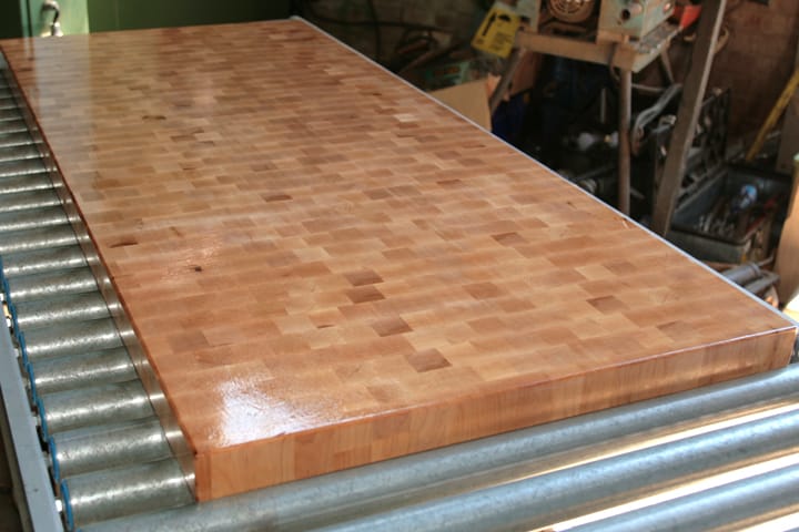 Freshly oiled end-grain butcher's block worktop gleaming on workshop rollers