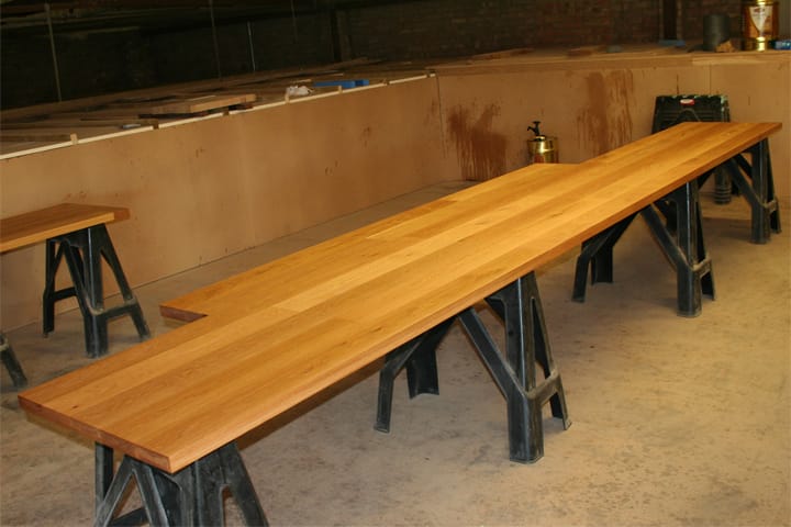 Long L-shaped oak worktop resting on cast iron trestles in the workshop