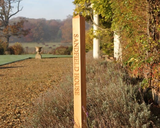 Engraved oak sign post reading Sandfield House in a country garden