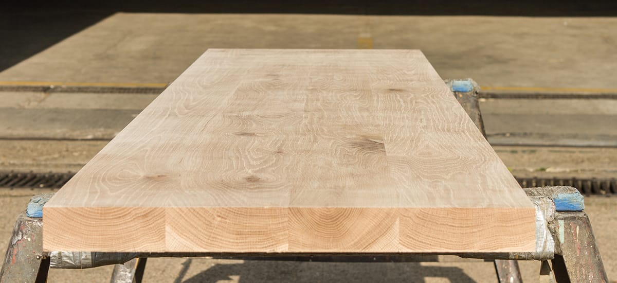 Unfinished character oak worktop with swirling grain resting on trestles outside the workshop