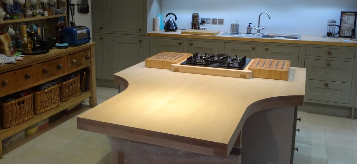 Curved maple island worktop with gas hob and butcher's blocks in a sage-green kitchen