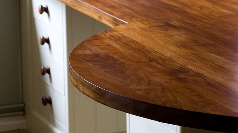 Rounded corner of a polished walnut worktop above cream painted drawers
