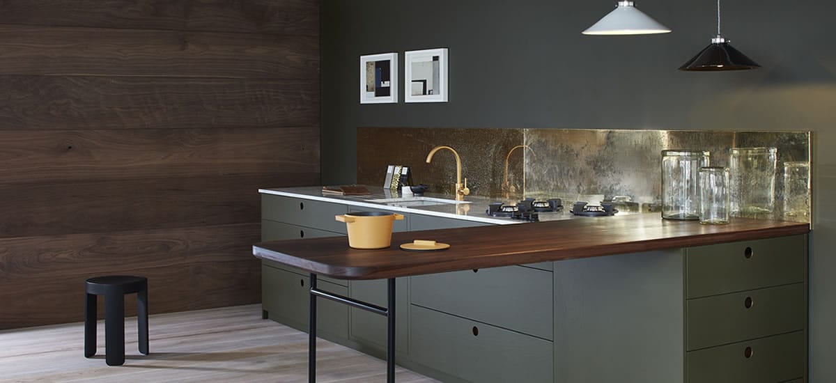 Walnut breakfast bar worktop on olive-green cabinets with a brass splashback
