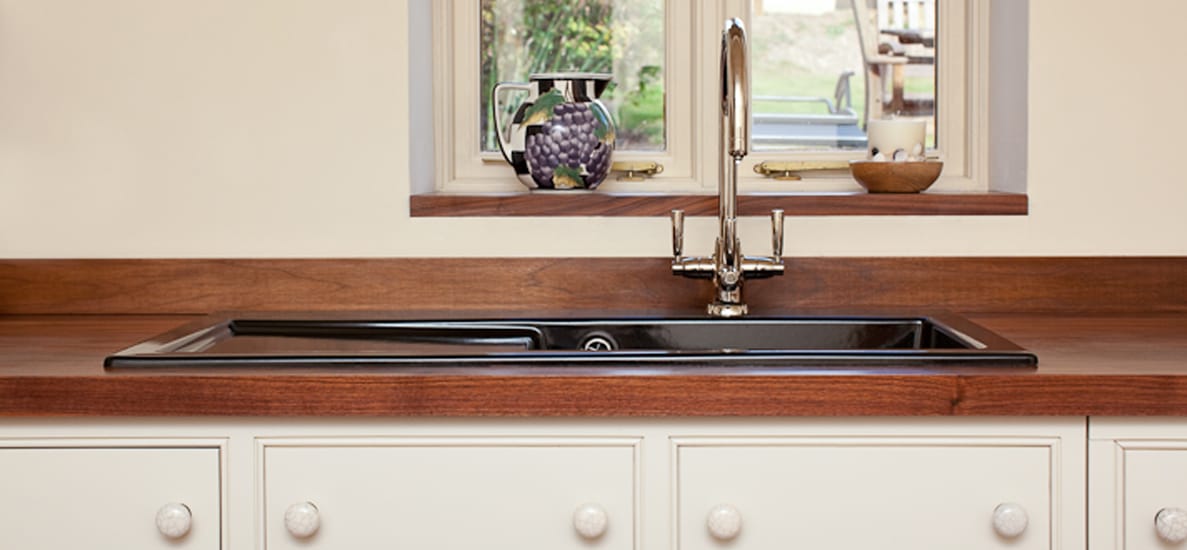 Walnut worktop with black inset sink and chrome tap beneath a cottage window