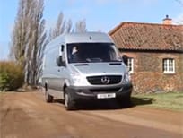 Silver Mercedes delivery van driving along a country lane past a brick cottage