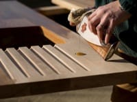Hands sanding a grooved wooden draining board in the workshop