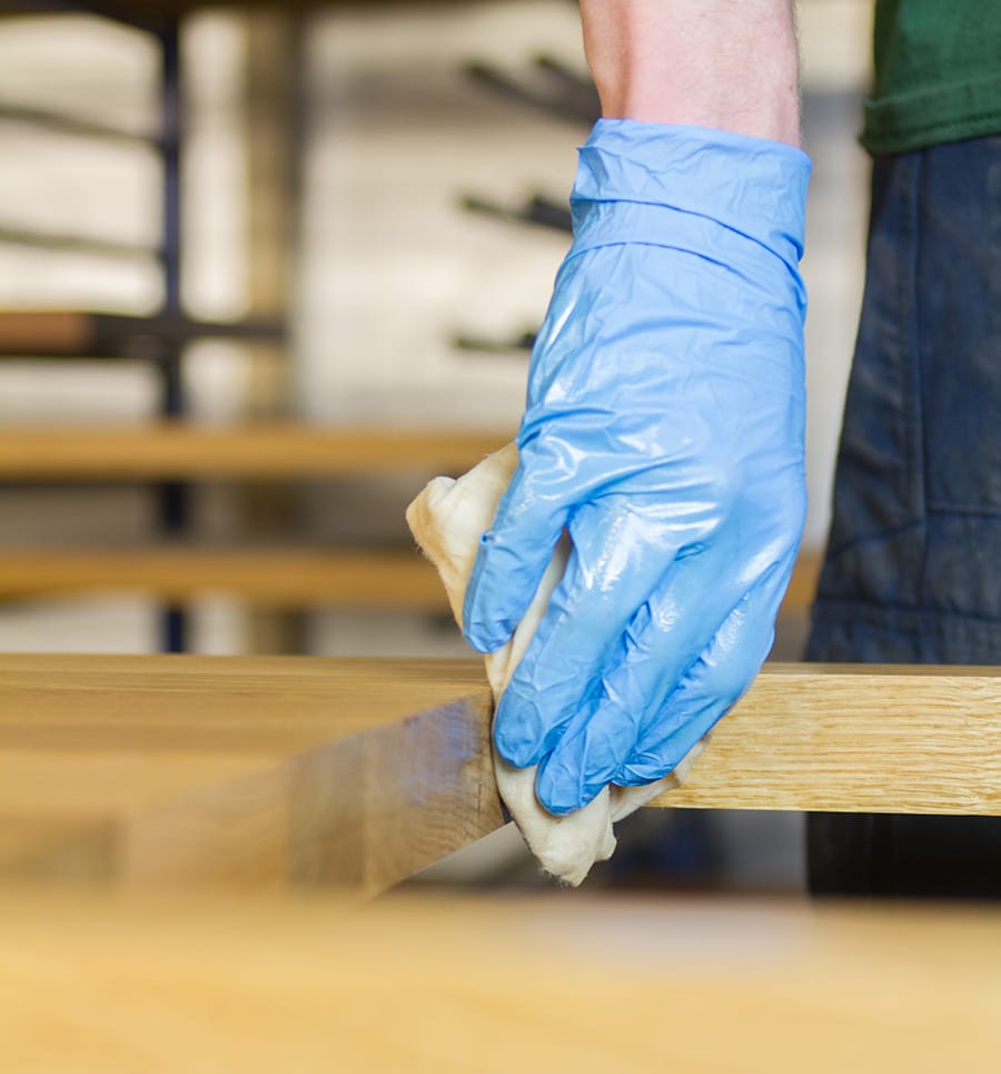 Worker in blue glove oiling the edge of an oak worktop in the workshop
