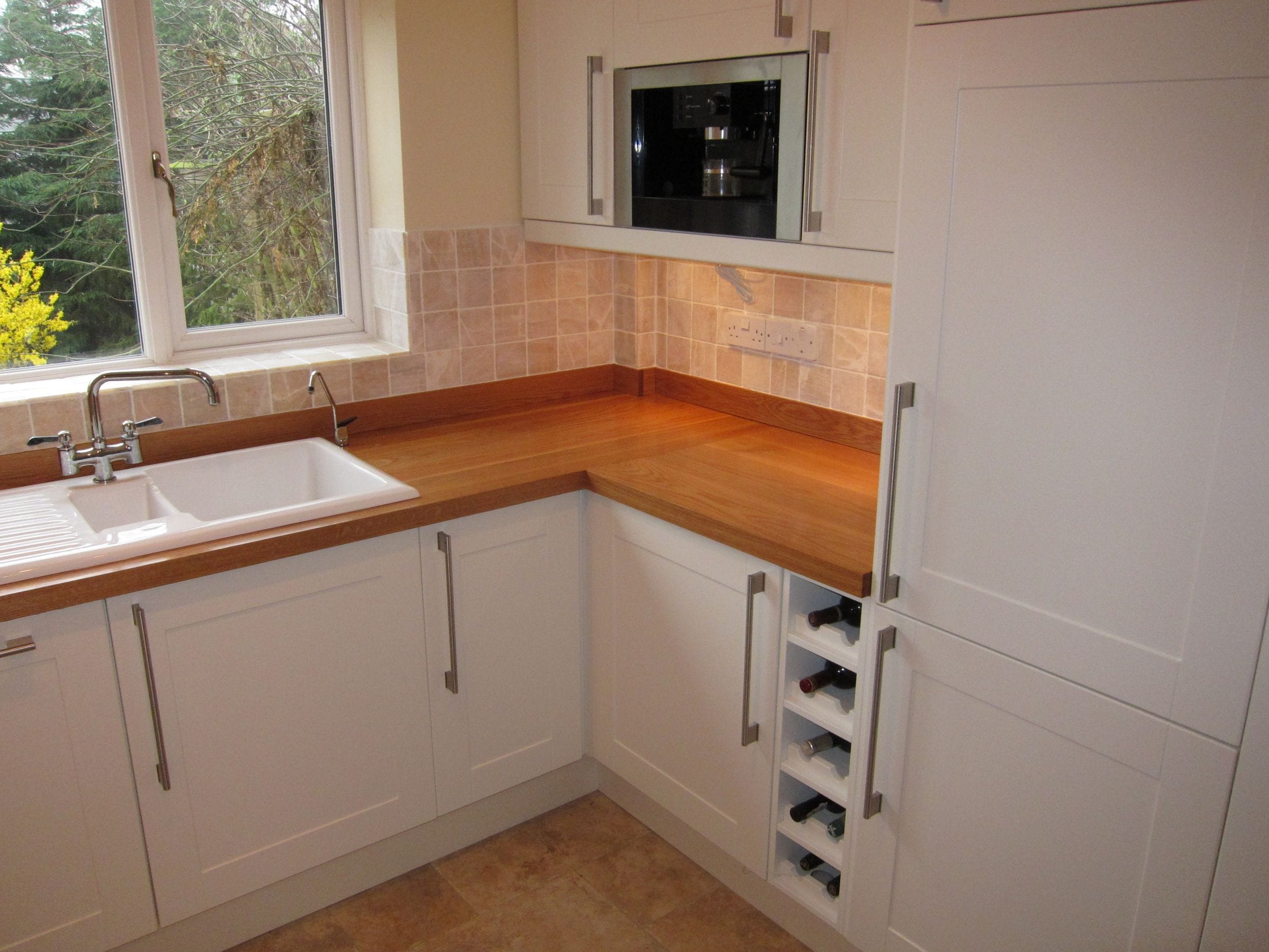 Oak worktops with upstands in a white shaker kitchen with ceramic sink and wine rack