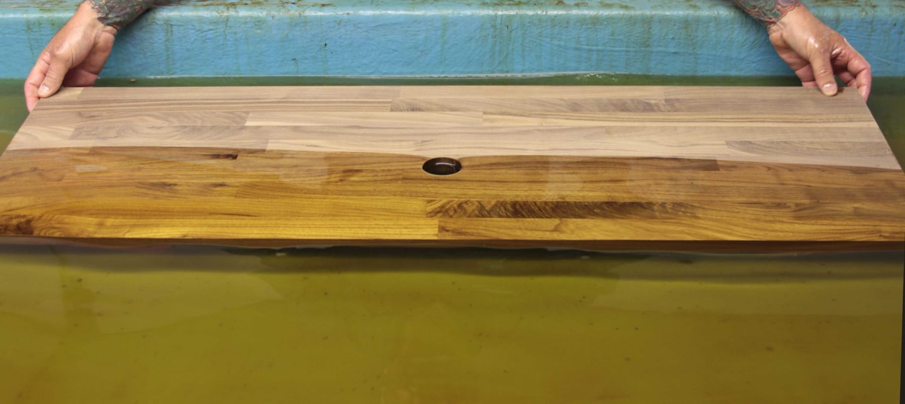 Walnut worktop being lowered into a tank of hot oil for pre-installation oiling