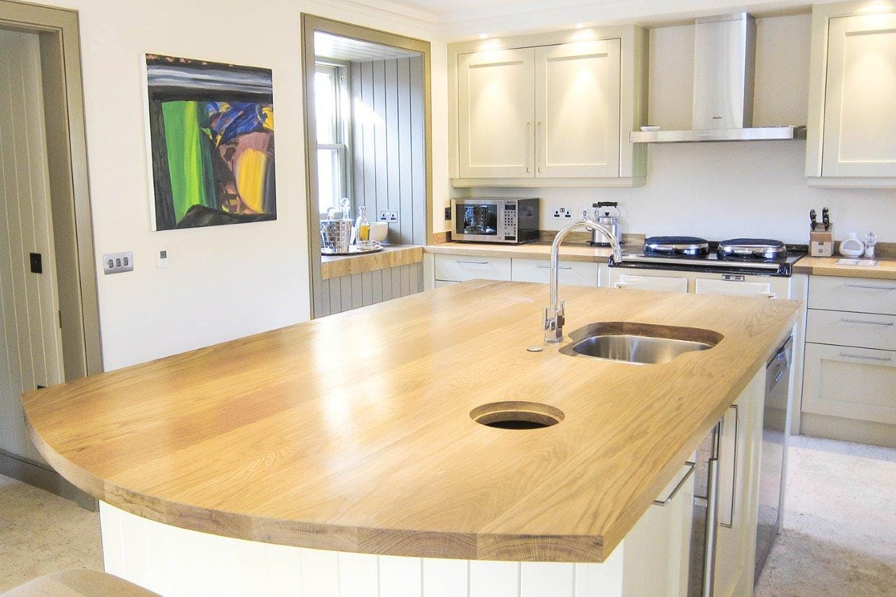 Curved oak island worktop with undermounted sink in a pale painted kitchen