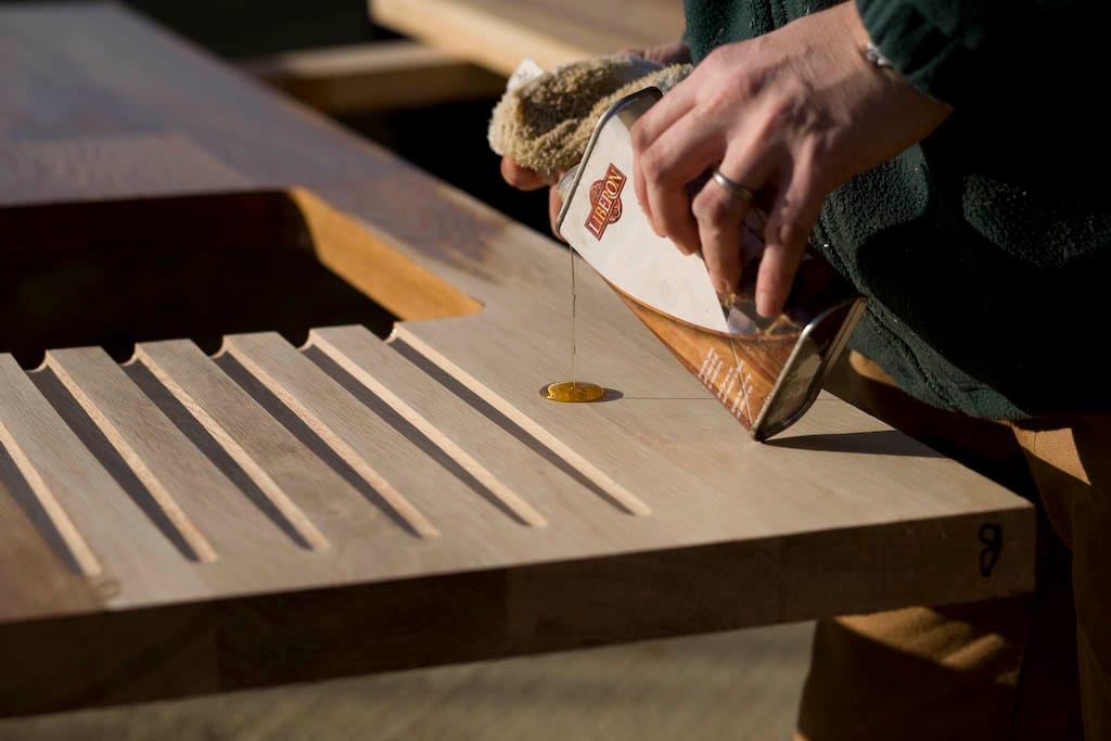 Tung oil poured from a tin onto an oak draining board section outdoors