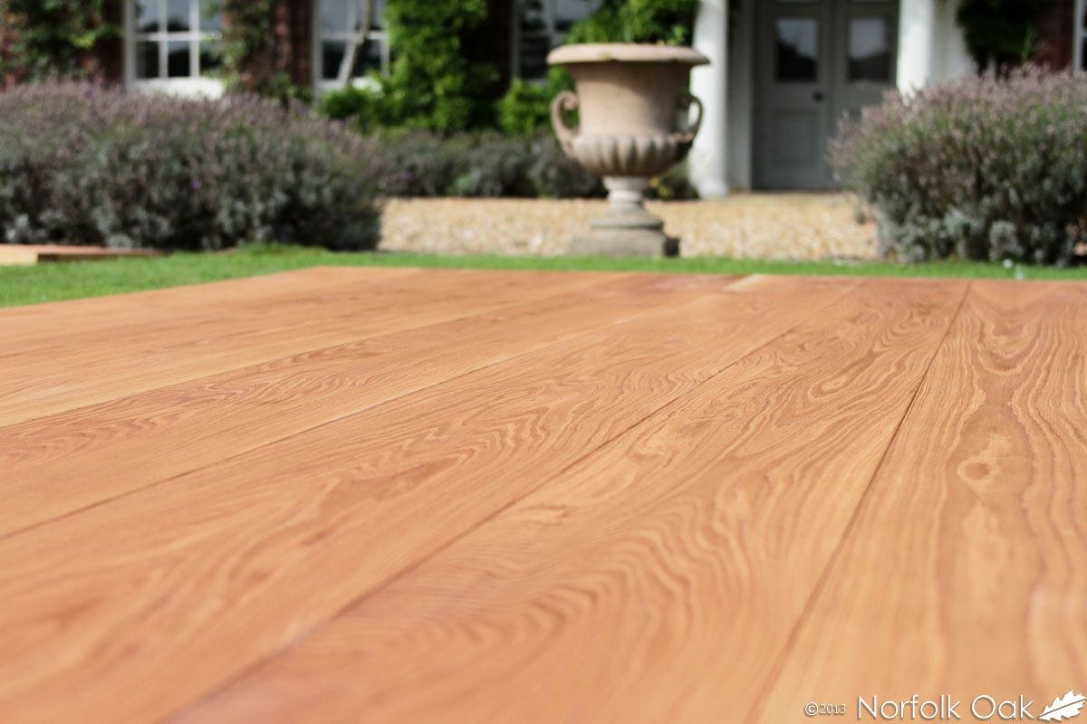 Close-up of oak floorboards laid outdoors with a stone urn and house behind