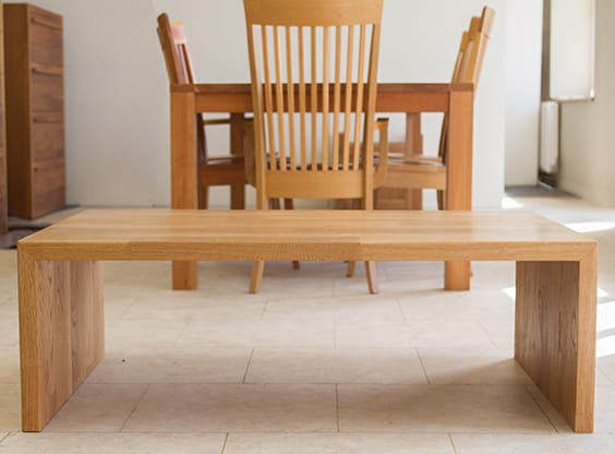 Large waterfall-style oak coffee table on a tiled floor in front of a dining set