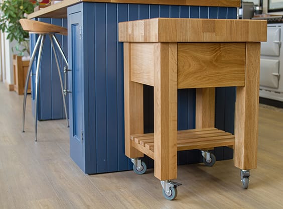 Oak end grain butcher block trolley on castors beside a blue kitchen island