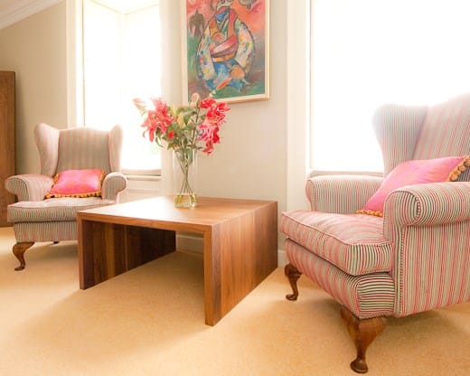 Modern walnut coffee table with flowers between two striped wing armchairs
