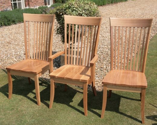 Three slat-back oak dining chairs, including a carver, on a lawn beside a gravel path